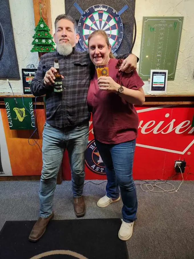Two darts players smiling together in front of a steel-tip dartboard