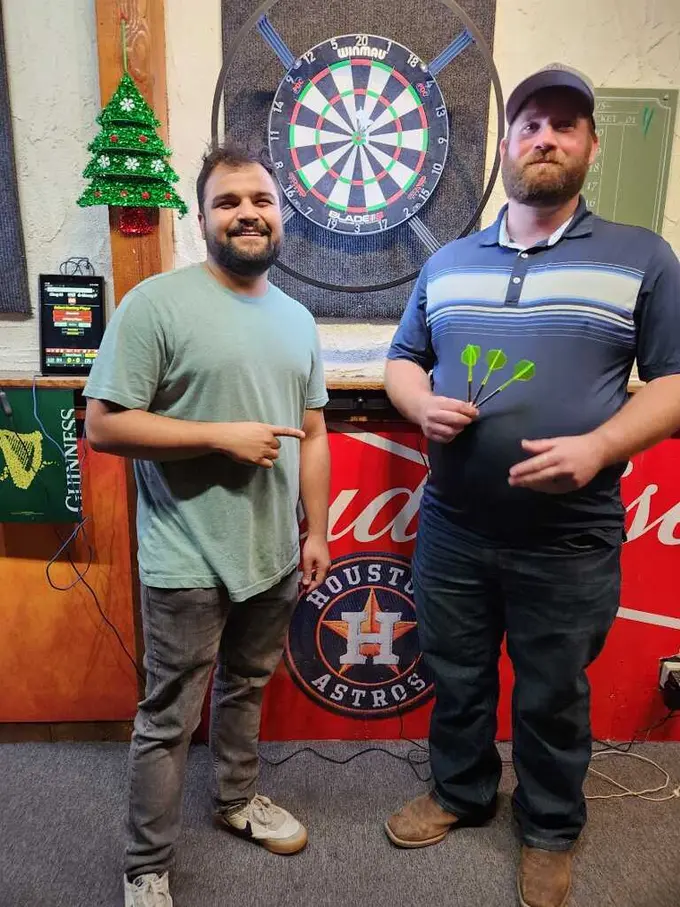 Two players holding darts in front of a dartboard at a Houston darts venue