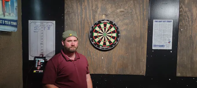 Darts player posing next to a dartboard in a Houston pub