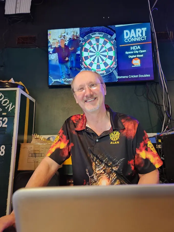 A darts player smiling in front of a lit electronic dartboard