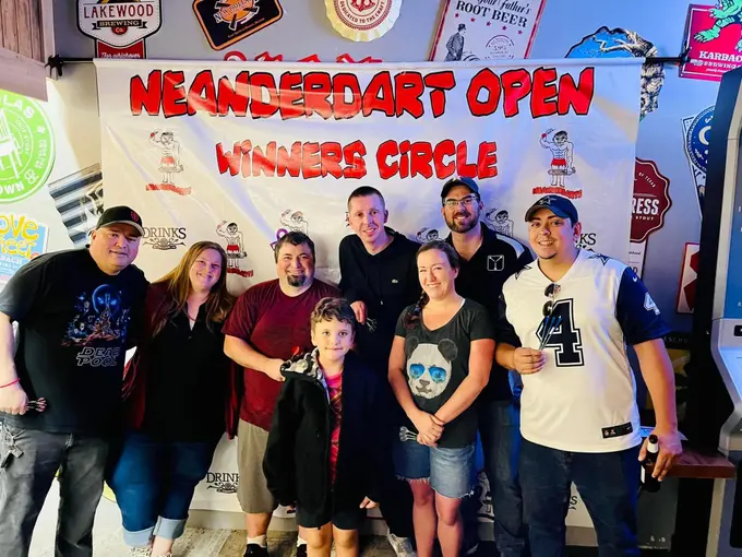 Group of darts competitors gathered in front of a tournament banner